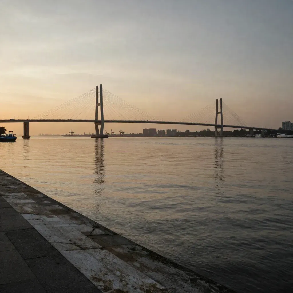 Siluet Jembatan Suramadu di tepi Surabaya saat senja, air dan kabut hangat.
